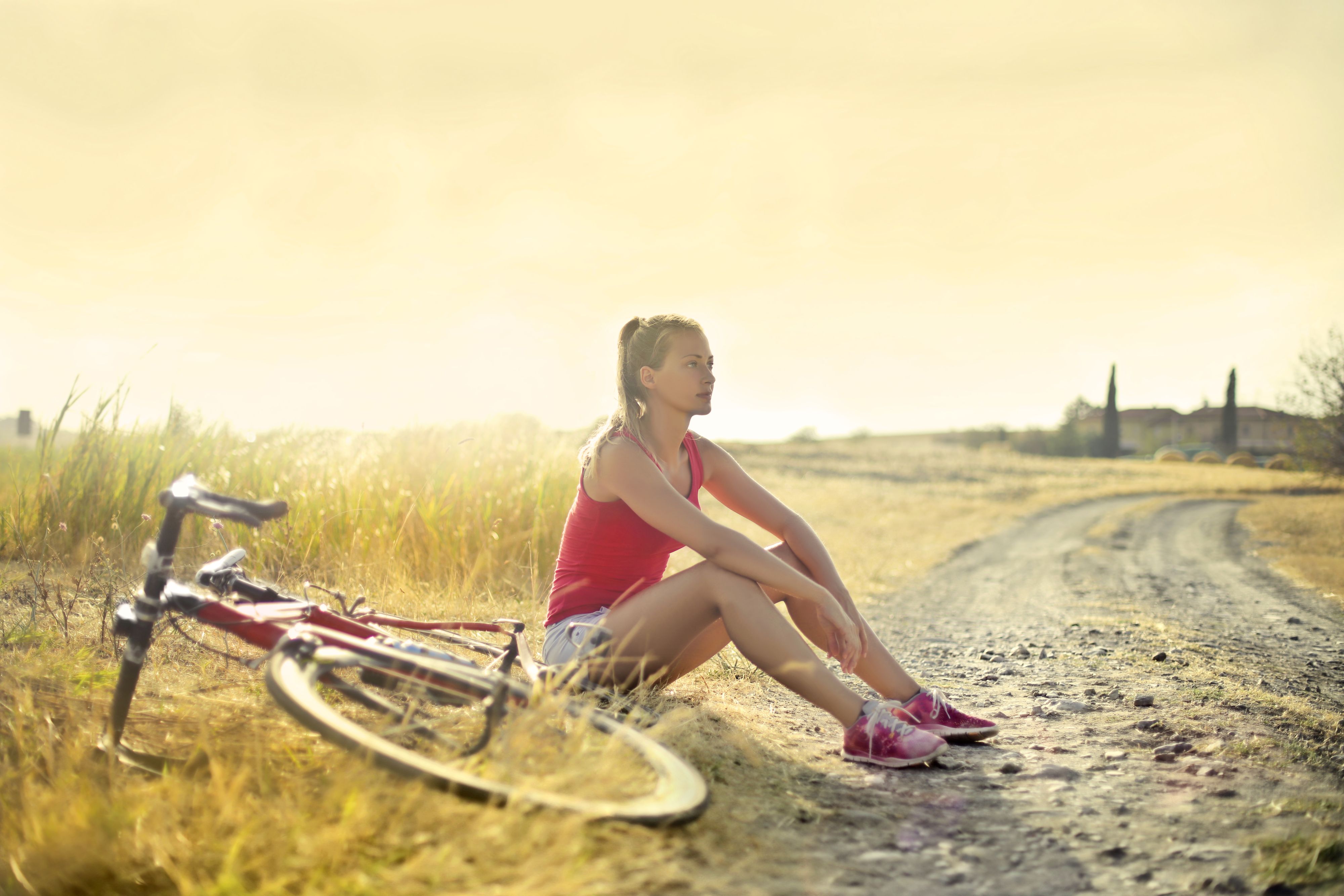 A woman sits beside her bicycle on a gravel roadside at golden hour.